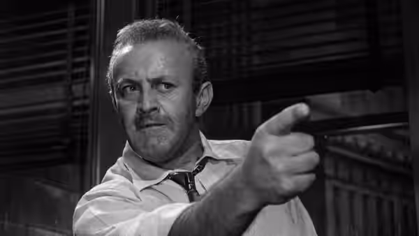 a man in a white shirt points forward with an intense expression