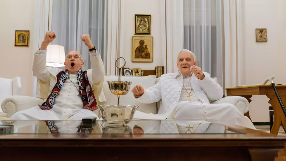 Pope Benedict XVI (Anthony Hopkins) celebrates beside Pope Francis (Jonathan Pryce) in a sitting room