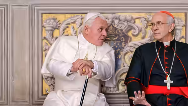 Pope Francis (Jonathan Pryce) speaks with Cardinal Bergoglio (Jonathan Pryce) beneath an ornate wall panel