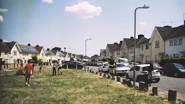 Children play on grass beside parked cars along a row of suburban houses