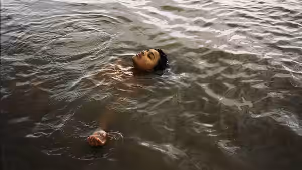 A young woman floats on her back in calm murky water with eyes closed
