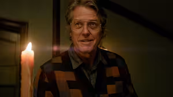 Mr. Reed (Hugh Grant) smiles beside a lit candle