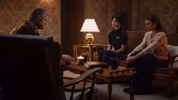 Mr. Reed (Hugh Grant) speaks with two women seated on a sofa