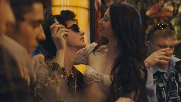Ivan (Mark Eydelshteyn) and Ani (Mikey Madison) smiling closely in a crowded bar