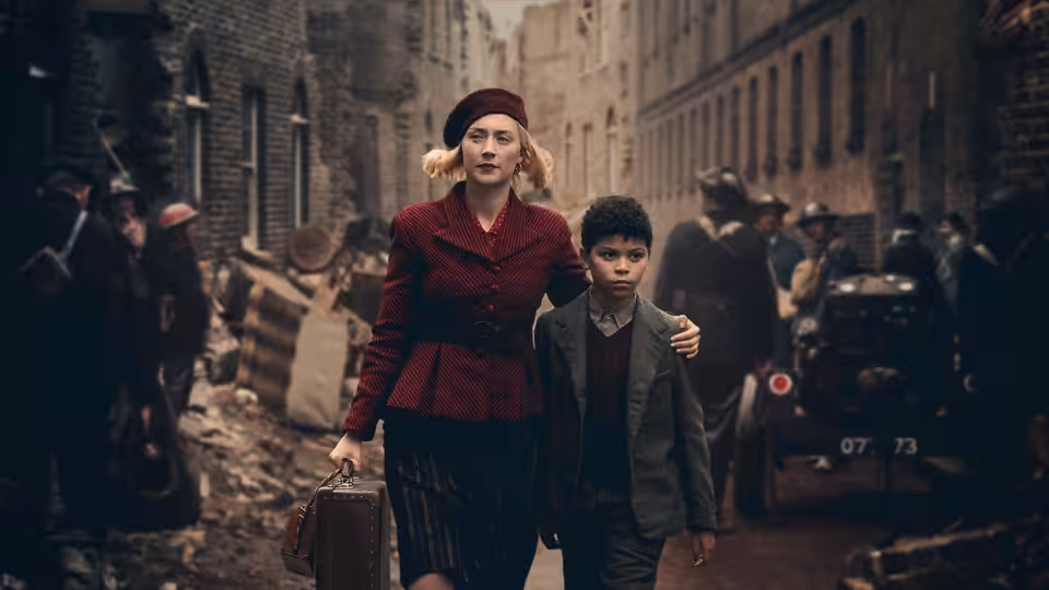 Rita (Saoirse Ronan) walking with George (Elliott Heffernan) through bombed streets
