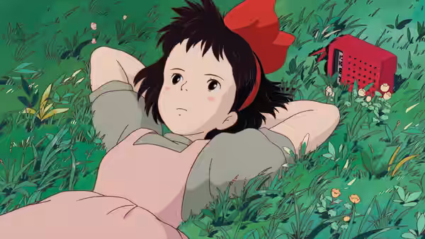Kiki (Minami Takayama) lying in a grassy field beside a red radio