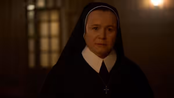 Sister Mary (Emily Watson) standing in a nun's habit in a dimly lit room