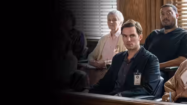 Nicholas Hoult as Justin Kemp sits in the jury box wearing a juror badge