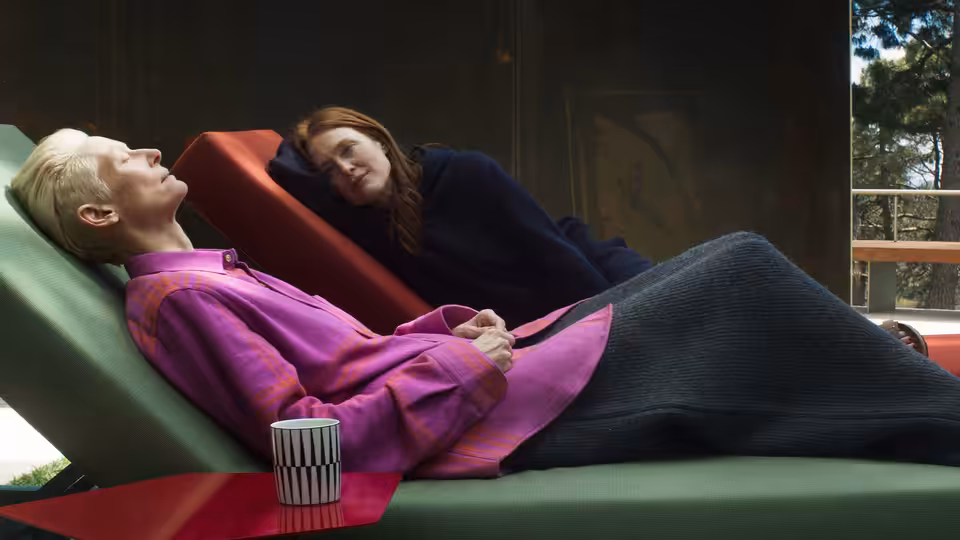Tilda Swinton reclines on a lounge chair beside Julianne Moore