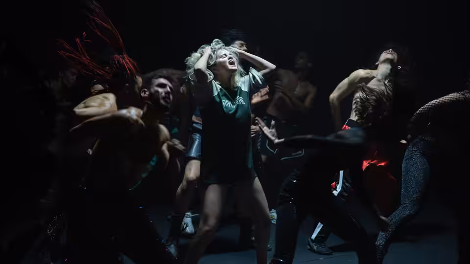 woman with green headpiece leading group of dancers in performance