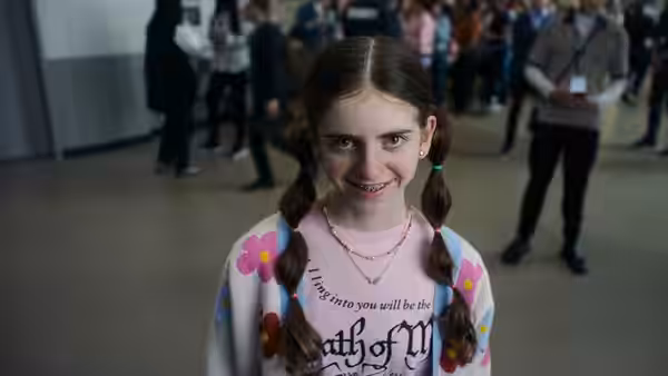Young girl with braided pigtails smiling in a crowded indoor space