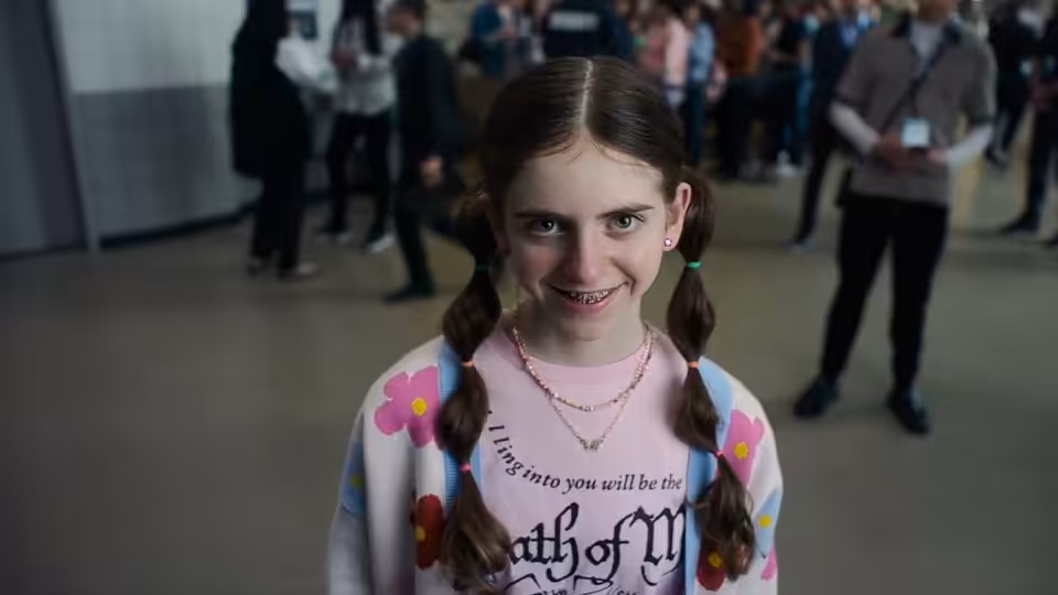 Young girl with braided pigtails smiling in a crowded indoor space