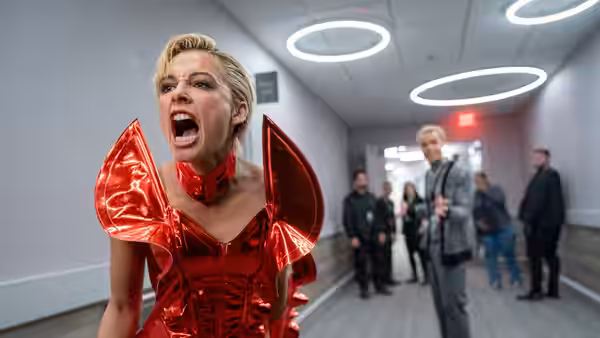 Skye Riley (Naomi Scott) shouting in a red metallic costume in a hallway