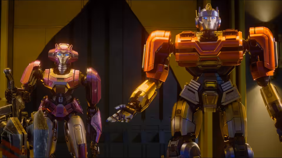Two robots stand inside a large metallic hall, one extending an arm