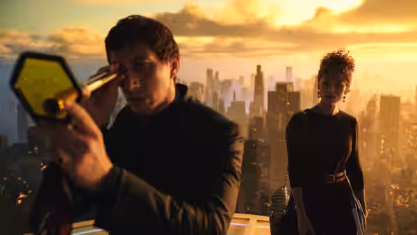 Man looks through a glowing device on a rooftop as a woman watches