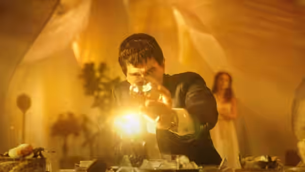Man holds a bright orb in a golden tent while a woman stands behind