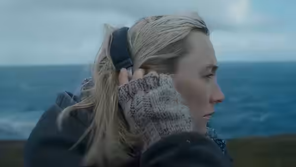 Rona (Saoirse Ronan) stands by the sea wearing headphones