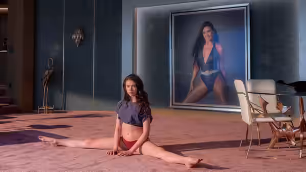 Sue (Margaret Qualley) doing splits on a pink rug before a poster of Elisabeth