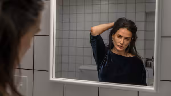 Elisabeth (Demi Moore) adjusting her hair while looking in a bathroom mirror