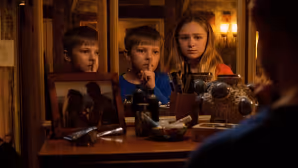 Three children at a vanity one holding a finger to lips