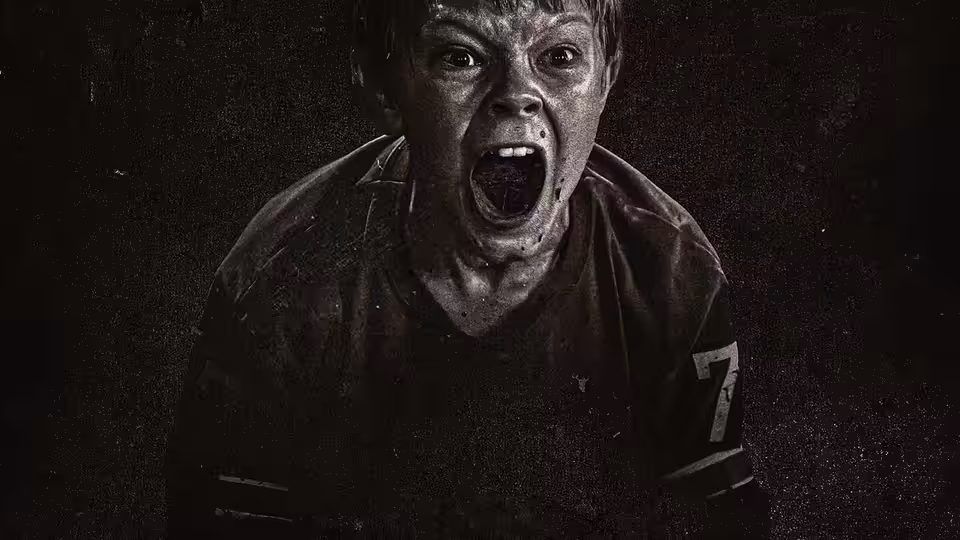 Boy in a dirty sports jersey shouts with mouth wide open