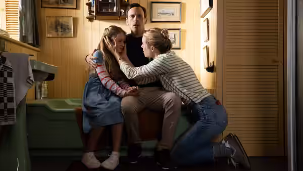Man and woman comfort a young girl on a living room couch