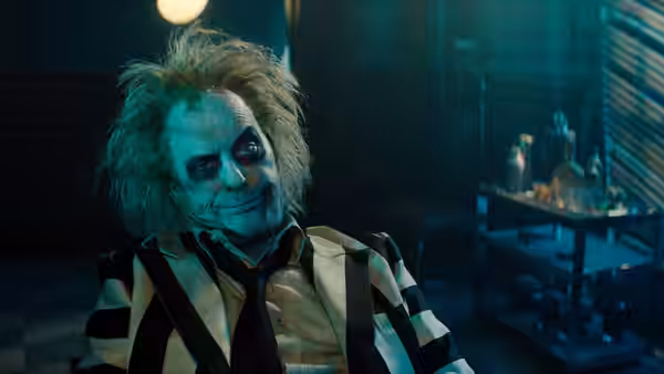 Beetlejuice (Michael Keaton) seated in a blue-toned room with a slight smile