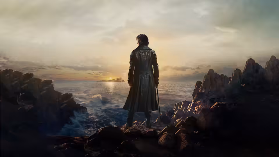 A man in a long coat stands on cliffs overlooking the sea at sunset