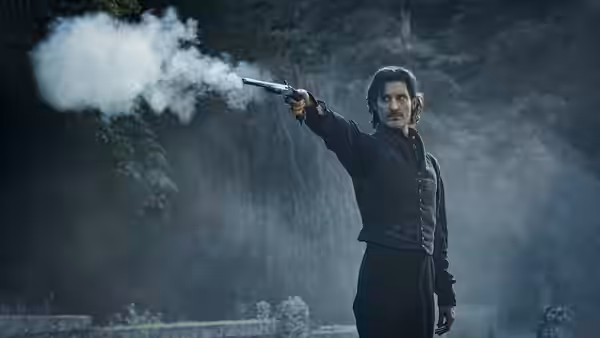 Pierre Niney as the Count fires a pistol in a misty wooded setting
