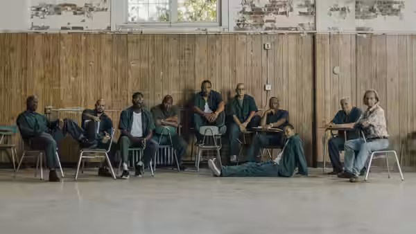 Men in green uniforms sit on chairs in a spacious hall with one lying down