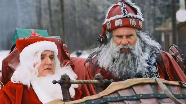 Santa (Bill Goldberg) sits beside another man in Santa costume on a sleigh