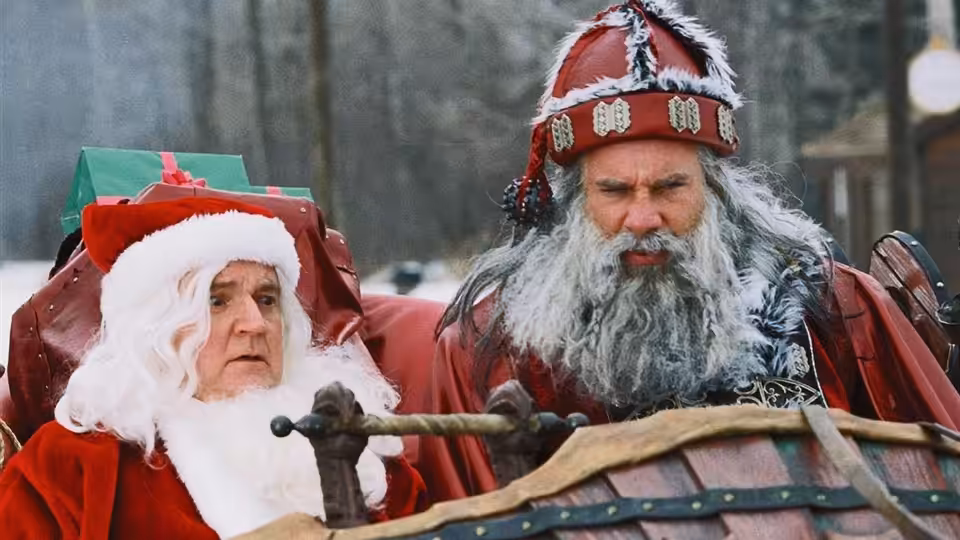 Santa (Bill Goldberg) sits beside another man in Santa costume on a sleigh