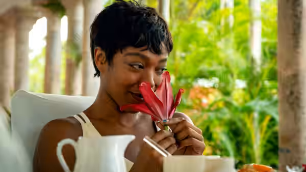 Frida (Naomi Ackie) smells a red flower while seated at a table