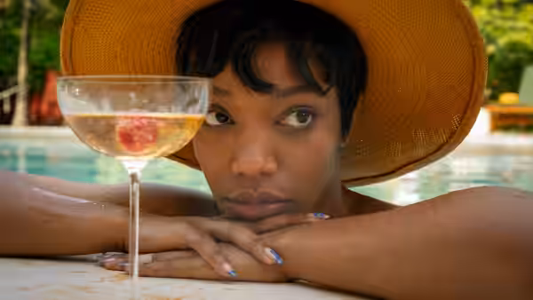 Frida (Naomi Ackie) rests her chin on her hands beside a cocktail