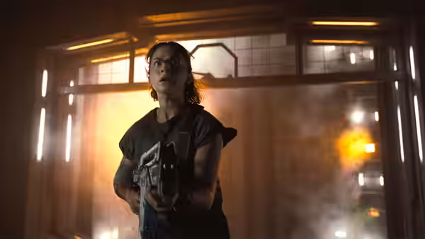 Rain (Cailee Spaeny) holding a gun in a smoky corridor
