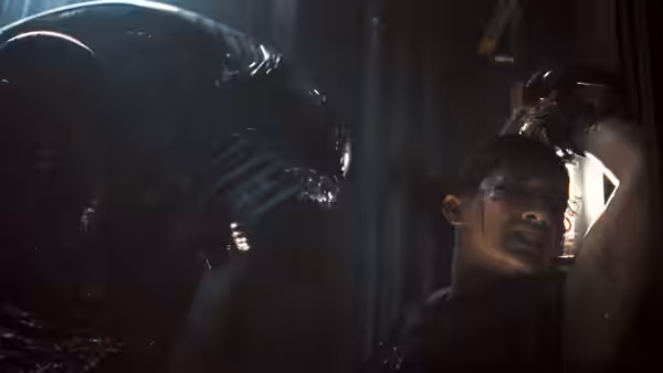Rain (Cailee Spaeny) facing a Xenomorph in a dark corridor