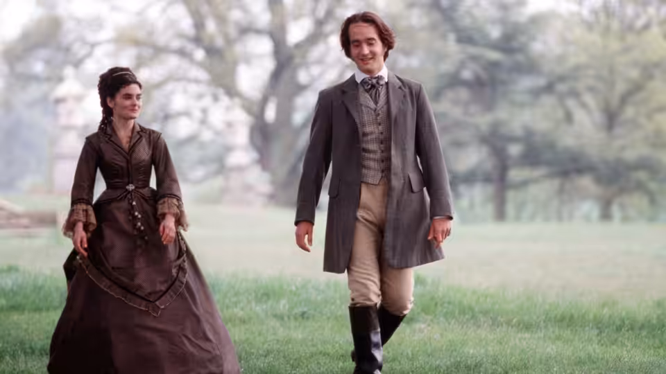 A woman and a gentleman walk together across a grassy park