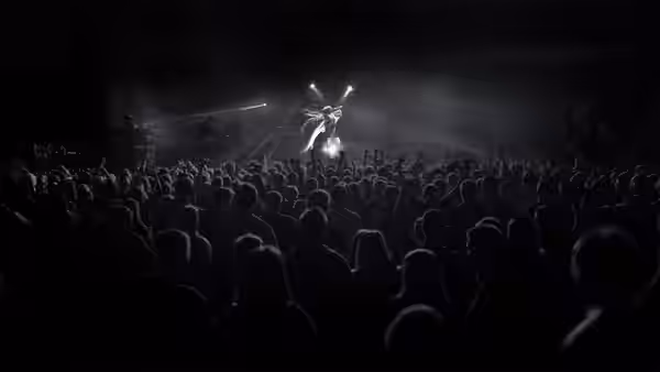 A performer on stage above a large crowd at a dark concert venue