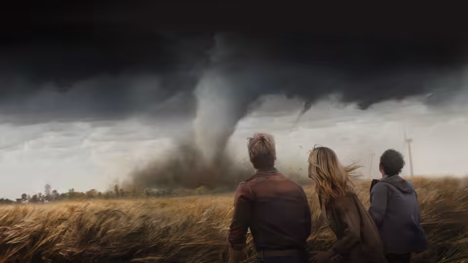 three people standing in a field watching a large tornado approach