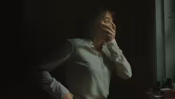 Agent Lee Harker covers her mouth while standing in a dim room