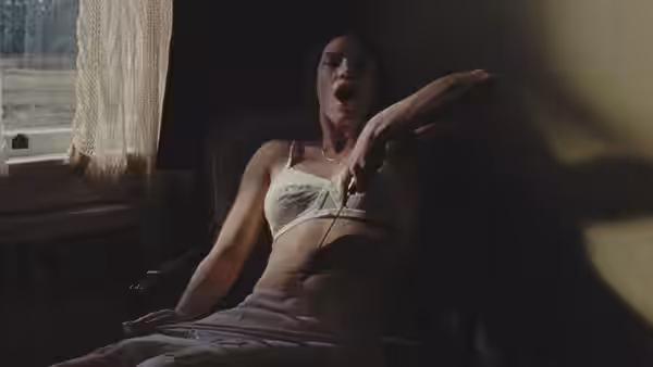A woman in a bra reclines in an armchair holding a handgun