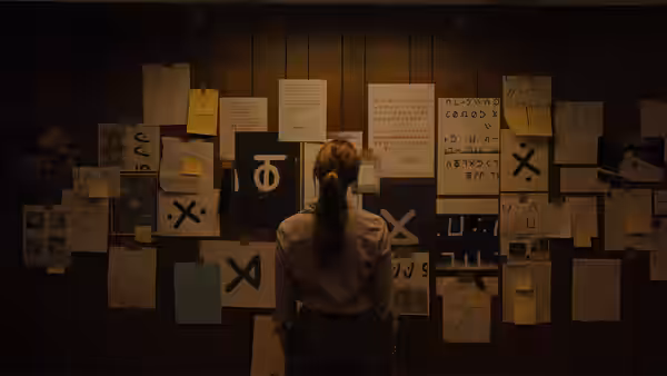 A woman stands facing a wall covered in papers and symbols