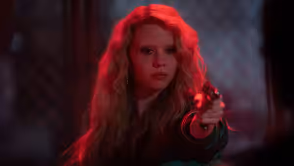 Maxine Minx (Mia Goth) pointing a gun forward in red light