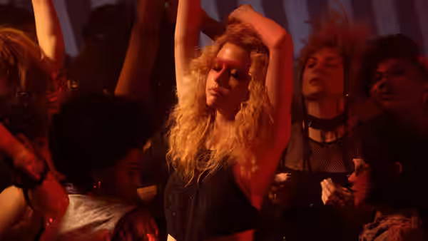 Maxine Minx (Mia Goth) dancing with arms raised in a crowded club