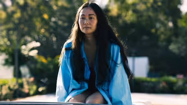 A woman with long dark hair sitting on a bench wearing a blue shirt