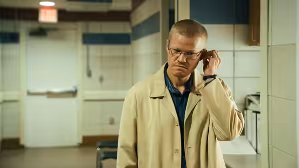 A man with glasses adjusting his ear while standing in a corridor
