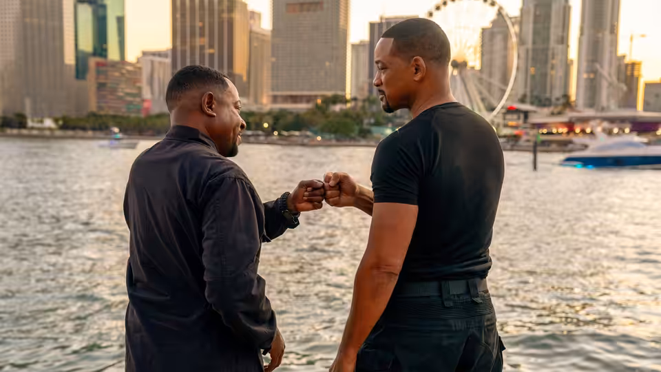 Mike Lowrey (Will Smith) and Marcus Burnett (Martin Lawrence) fist-bumping by the waterfront at sunset