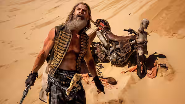 a bearded warrior standing beside a wrecked motorcycle in the desert