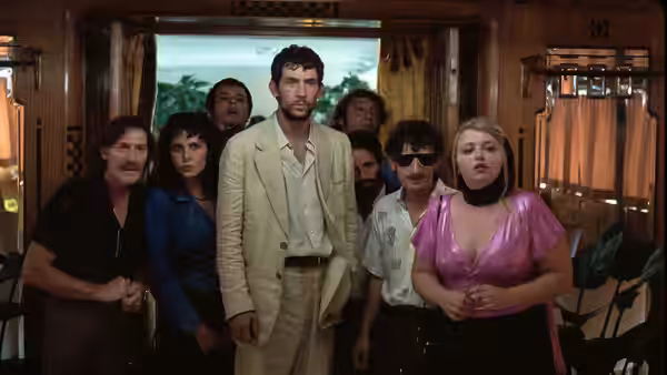 Arthur (Josh O'Connor) standing with several people inside a train carriage