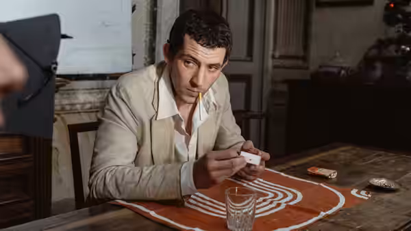 Arthur (Josh O'Connor) holding a card with a cigarette at a wooden table